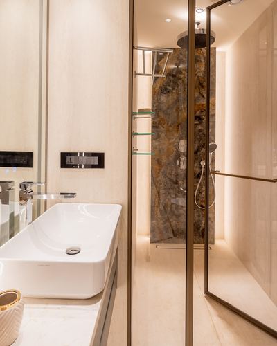 Bathroom with white vessel sink and glass-enclosed shower featuring veined stone wall