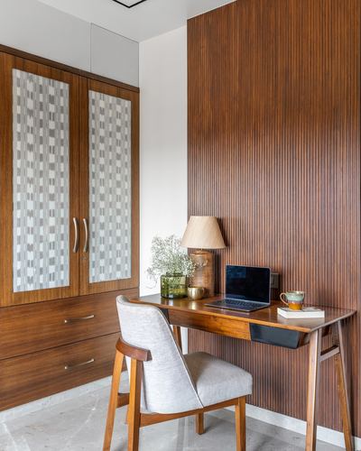 Study nook with fluted wood wall, wooden desk, laptop, and patterned wardrobe in Pune home