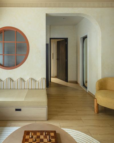 Living room with round terracotta window, scalloped bench, arched hallway, and mustard chair