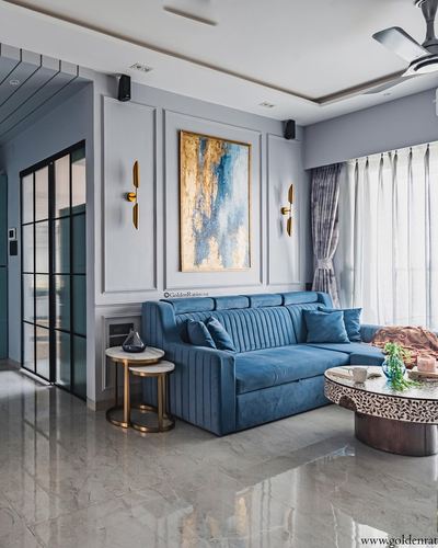 Blue velvet sofa in living room with paneled wall, gold sconces, and abstract art above.