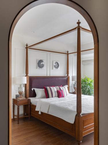 Four-poster wooden bed with maroon leather headboard seen through an arched doorway