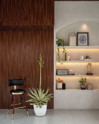 Fluted dark wood wall beside a lit arched shelving niche with plants and a bar stool.