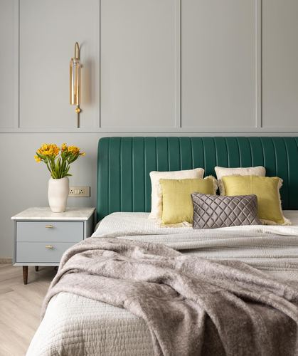 Bedroom corner with green tufted headboard, marble-top nightstand and brass wall sconce
