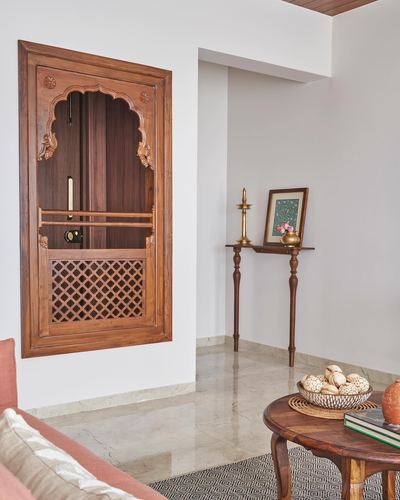 Carved wooden traditional door in white wall beside slender console table with brass diya, in Pune living room