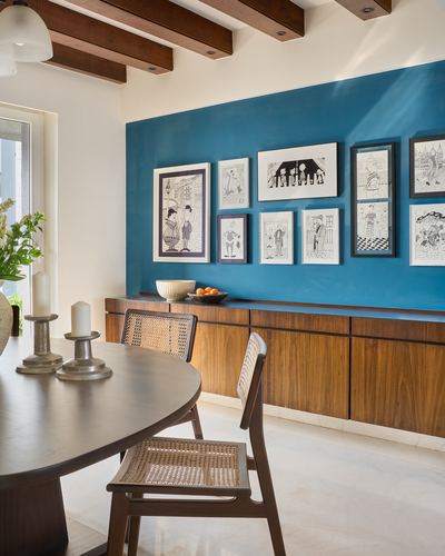 Dining room with teal accent wall, framed illustrations, wood sideboard and cane-back chairs