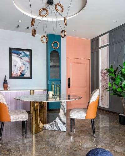 Round marble dining table with brass base, orange leather chairs, teal cabinet and peach door behind