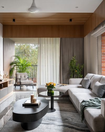 Grey sectional sofa and oval black coffee table in a wood-ceilinged living room opening to a green balcony
