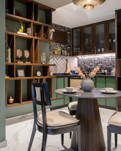 Dining nook with fluted pedestal table, cane chairs and wooden display shelving beside green kitchen
