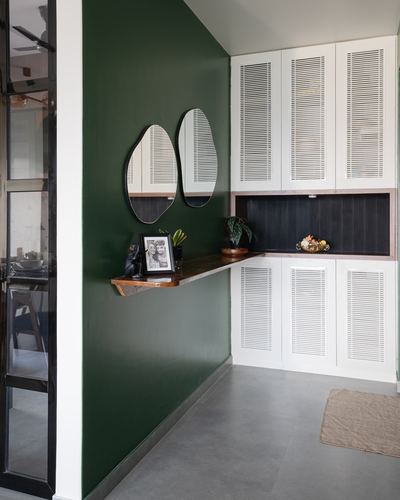 Green-walled foyer with two round mirrors over a wood console and white louvered storage