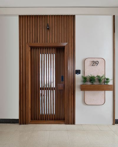 Entrance door with vertical wood fluting beside a pink number plaque with planters, unit 29