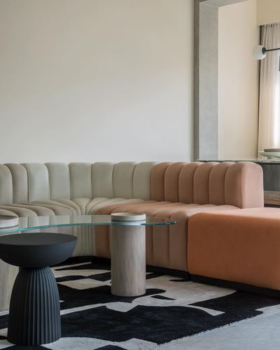 Curved channel-tufted sofa in beige and terracotta with glass table on black and white rug