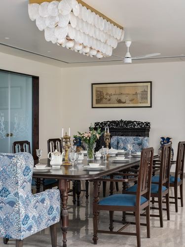 Formal dining room with long wood table, blue-patterned chairs, carved screen and capiz shell chandelier