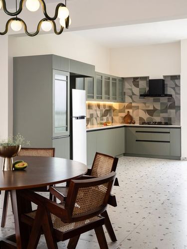 Sage green kitchen with patterned tile backsplash, terrazzo floor, and cane dining chairs in foreground