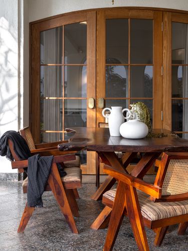Wooden dining table with cane chairs on terrazzo floor before arched wooden glass doors