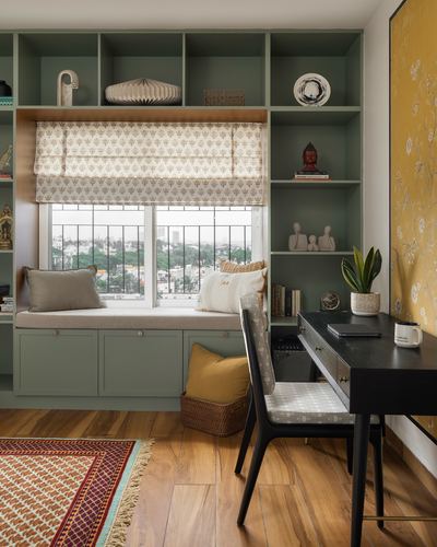 Sage green built-in shelving with window seat and black desk in a study nook