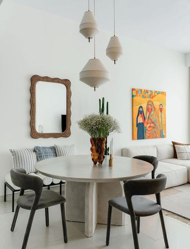 Round stone dining table with grey chairs beneath layered pendant lights, colorful artwork on wall