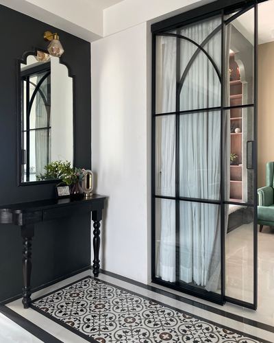 Foyer with black wall, arched mirror over black console, and tall black-framed glass door with sheer curtain