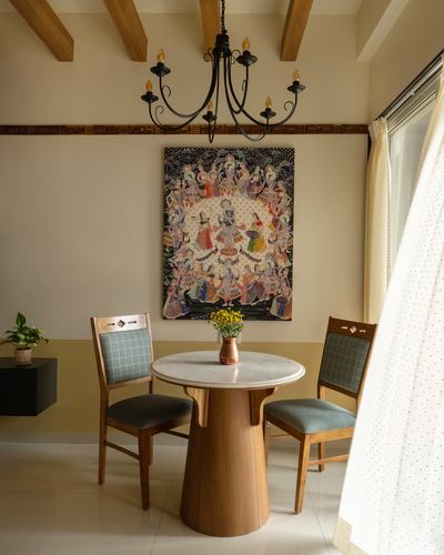 Dining nook with round marble table, chandelier, and Pichwai painting on wall