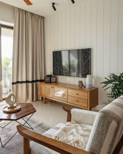 Living room with wood-panelled wall, TV console, cane armchair and linen curtains