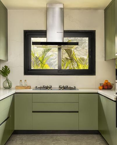 U-shaped olive green kitchen with black-framed window and stainless steel chimney hood above hob