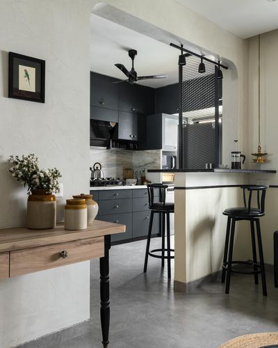 Kitchen seen through plastered archway with black cabinetry, marble backsplash, and bar seating at counter