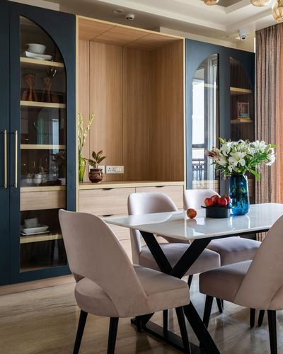 Dining area with marble table, blush velvet chairs, and navy arched glass cabinets