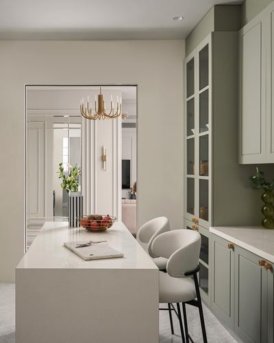 Sage green kitchen island with white countertop, glass-front cabinets, view through archway to chandelier