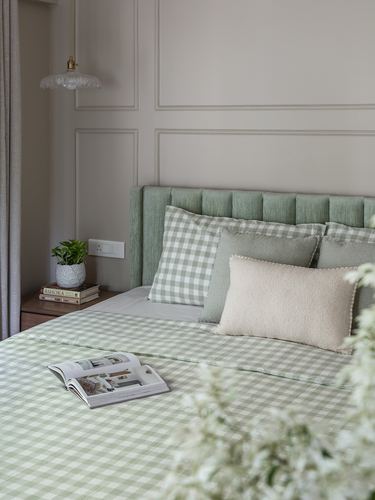 Bed with green tufted headboard, gingham linens, and mixed pillows against panelled wall