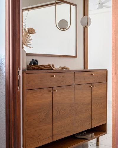 Wooden console with brass knobs and mirror seen through a doorway