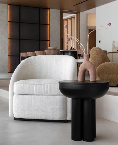 White boucle armchair beside black sculptural side table with ceramic vase, backlit dark grid wall behind