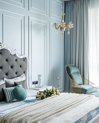 Powder blue bedroom with tufted grey headboard, crystal chandelier, and teal wire-frame chair