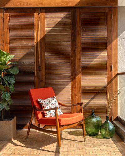 Orange mid-century armchair against wooden louvered shutters with glass bottles and a plant on a balcony