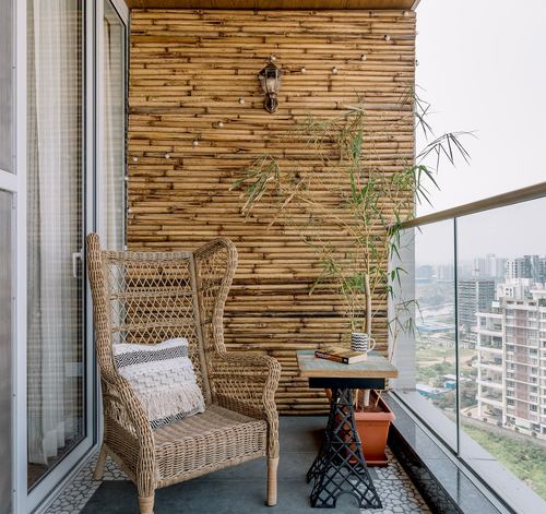 Balcony with wicker wingback chair against bamboo-clad wall and city view