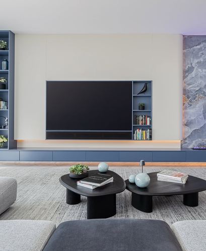 Modern living room with cream and blue-grey media wall, built-in shelving, and organic black coffee tables