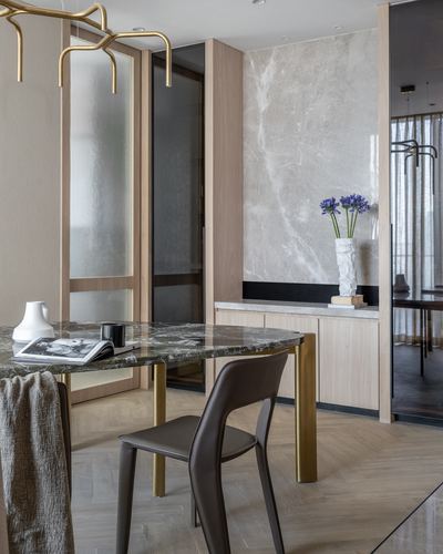 Dining area with green marble table, brass legs, leather chair, and marble-clad wall with console.