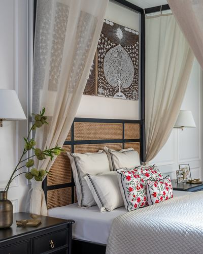 Bedroom corner with black four-poster bed, cane headboard, sheer curtains, and framed tribal-motif artwork.
