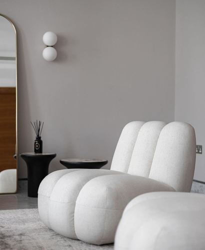 Cream channel-tufted lounge chair and ottoman beside black side tables and a gold-framed mirror