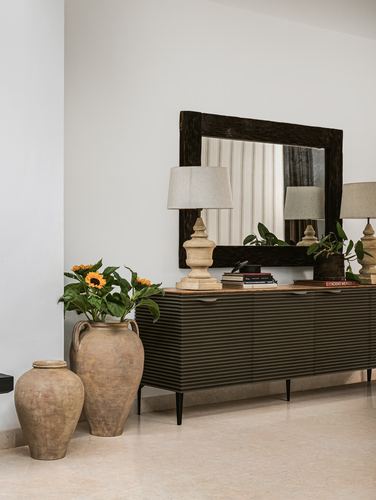 Fluted dark console with mirror, lamps, books and ceramic urns with sunflowers in a foyer