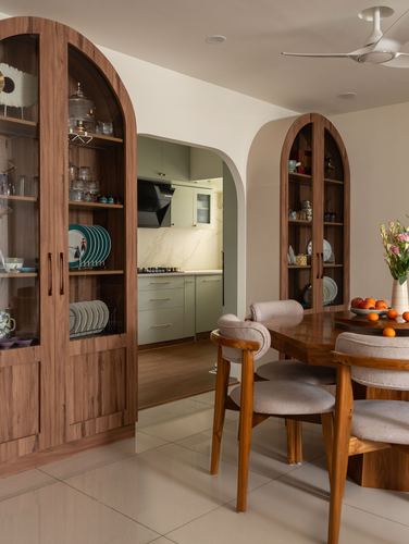 Dining room with arched wooden display cabinets flanking a table, opening to a sage green kitchen beyond
