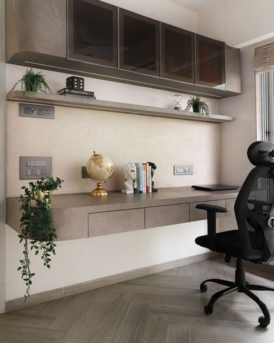 Floating stone desk with globe, books, and bust under overhead cabinets, black ergonomic chair, herringbone floor