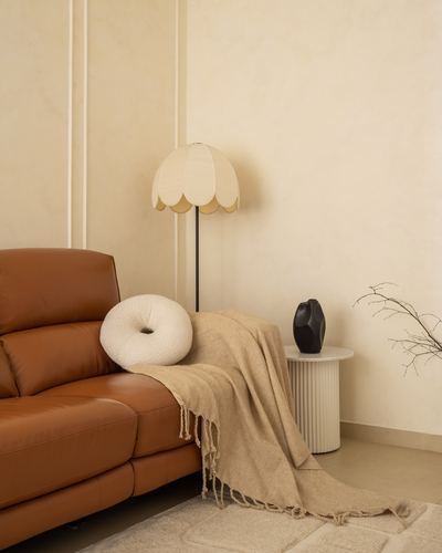 Corner of living room with tan leather sofa, scalloped floor lamp, and fluted side table