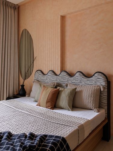 Bed with scalloped upholstered headboard against terracotta fluted wall and round mirror