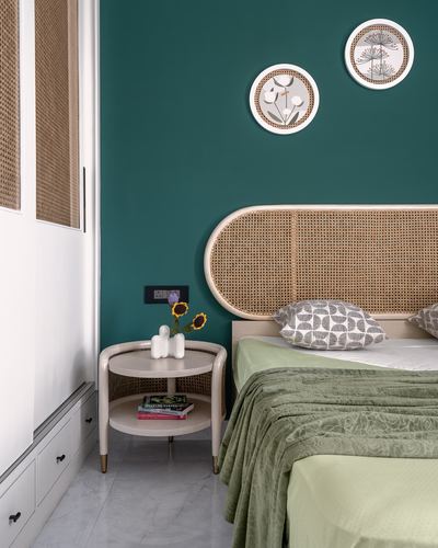 Bedroom corner with teal wall, cane headboard, round side table and sage green bedding