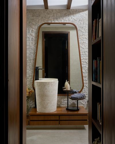Doorway view of a bathroom with a stone cylindrical basin under a tall arched mirror