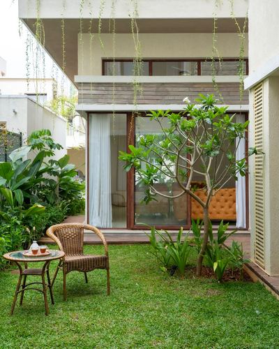 Garden facade with wicker chair, tea table, frangipani tree, and glimpse of orange sofa inside