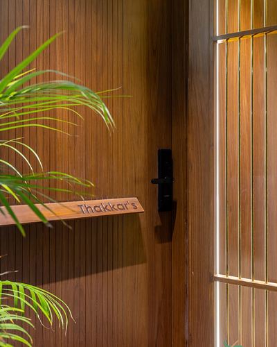 Close-up of a fluted wood entrance door with 'Thakkar's' nameplate and vertical light strip