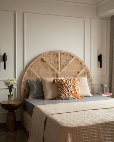 Bed with arched cane headboard against white paneled wall, styled with neutral pillows and flowers