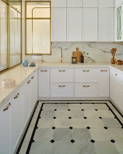 White L-shaped kitchen with marble backsplash, brass hardware, and patterned marble floor with black inlay