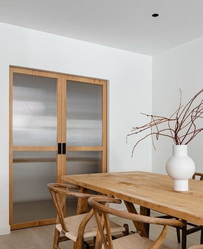Dining nook with wishbone chairs, wood table, white vase and reeded glass timber doors