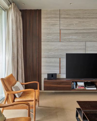 Living room with stone-clad tv wall, wood fluted panel, and tan leather armchair by window